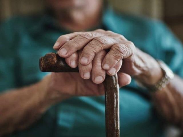 Older person sitting down holding a walking stick